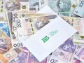 Koperta ZUS na stosie polskich banknotów. Może to być symbol wypłaty zasiłku przedemerytalnego lub innych świadczeń.