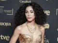 Mujer con espectacular pelo rizado, peinado con volumen y brillo. Luce un vestido dorado y un collar de cadenas.