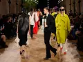 Sfilata Balenciaga: modelli con abiti audaci, tra cui un cappotto giallo acceso e un completo nero, sotto gli occhi del pubblico.