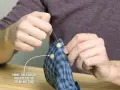 Main tenant une chemise à carreaux bleus, il est en train de coudre un bouton avec une aiguille et du fil blanc.