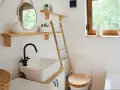 Bagno piccolo con piastrelle bianche lucide, lavabo squadrato, specchio rotondo e scala in bambù. Idee piastrelle bagno piccolo: la luminosità è la chiave.