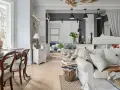 Un salotto con un'atmosfera da arredamento francese chic. Tavolo da pranzo in legno, divano bianco accogliente, lampade e decorazioni rustiche.