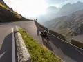 Motocyklista przemierza serpentyny górskiej drogi, odkrywając najpiękniejsze trasy motocyklowe w Europie. Słońce przebija się przez mgłę, oświetlając majestatyczne szczyty.