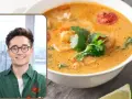 Uśmiechnięty mężczyzna w okularach prezentuje aromatyczną zupę tajską z krewetkami i pomidorkami, ozdobioną świeżą kolendrą.