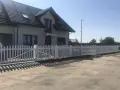 Biały płotek ogrodowy zrób to sam, idealnie otacza dom. Wygląda jak nowy, dodaje uroku posesji.