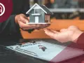 Manos entregan una maqueta de casa sobre un contrato y llaves. El IVA del alquiler de un local se desgrava.