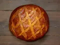 Ein **freigeschobenes Brot** mit knuspriger Kruste und Rautenmuster liegt auf dunklem Holz.