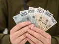 Dłonie trzymają polskie banknoty: 100 i 200 zł. To symbol nagrody za pracę, jak 800 plus tylko dla pracujących.