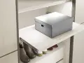 Un ripiano estraibile fai da te, con una scatola grigia sopra e scarpe sotto, ottimizza lo spazio in un armadio moderno.