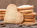 Szybkie kruche ciasteczka w kształcie serca i okrągłe, posypane cukrem, leżą na drewnianym blacie obok ziaren kawy.