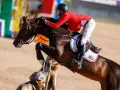 Le cheval Balou du Reventon saute un obstacle, son cavalier en veste rouge le guidant avec précision.