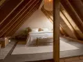 Accogliente camera da letto in un **sottotetto bassissimo**, con travi in legno a vista e un letto bianco immacolato.