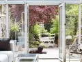 Gemütliches Wohnzimmer mit Blick in den Garten. Ein Hund liegt auf der Holzterrasse, ideal zum Wintergarten einrichten.