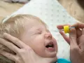 Ein Baby weint, während ihm N सेंटropfen verabreicht werden.