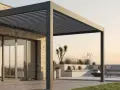 Una moderna casa con una **pérgola bioclimática** que ofrece un espacio exterior acogedor con asientos, tumbonas y una hoguera.