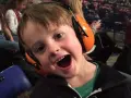 Un jeune garçon de 3 ans, avec un bouchon oreille enfant 3 ans, sourit à pleines dents, prêt pour le spectacle.