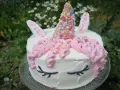 En förtrollande unicorn tårta med rosa glasstrut-liknande horn, dekorerad med strössel och blommor i bakgrunden.