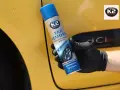 Rękawiczka z czarną gumą trzyma puszkę K2 Tar Remover, która skutecznie usuwa smołę z żółtego lakieru samochodu.