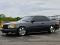Ciemnoszary Mercedes "Hammer" coupe z przyciemnianymi szybami i chromowanymi felgami stoi na mokrej drodze.