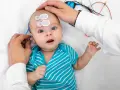 Badanie słuchu u niemowlaka. Czy niedosłuch u dziecka można wyleczyć? Lekarz bada malucha, zakładając elektrody na głowę.