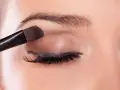 Application d'un fard à paupières marron pour un regard smoky intense.