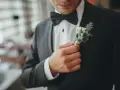 Mężczyzna poprawia butonierkę w eleganckim, czarnym garniturze.