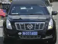 Czarny Cadillac z amerykańską flagą i tablicą rejestracyjną CD W-001600, wskazującą na rejestracje dyplomatyczne.