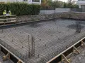 Costruzione di una platea di fondazione con rete metallica e armature in vista. Due operai con caschi discutono il progetto.