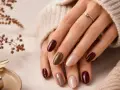 Mani curate con smalti color terra e bordeaux, un'anticipazione delle unghie inverno 2026. Un anello dorato completa il look.