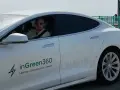 Uśmiechnięty mężczyzna w okularach przeciwsłonecznych siedzi za kierownicą białej Tesli z logo inGreen360.