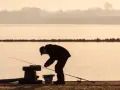 Wędkarz przygotowuje zanętę do koszyczka nad spokojną wodą o zachodzie słońca.