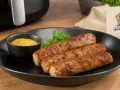 Drei goldbraune Bratwürste im Airfryer zubereitet, serviert mit Senf und Petersilie auf einem schwarzen Teller.