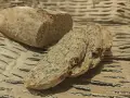 Chleb orkiszowy, pokrojony w kromki, z widocznymi ziarnami, leży na falistej tekturze.