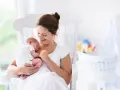 Uśmiechnięta mama kołysze śpiące dziecko. Gratulacje z okazji narodzin dziecka!