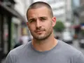 Un pelado hombre con barba corta mira a la cámara, con una calle borrosa de fondo.