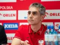 Trener reprezentacji Polski w piłce ręcznej, w czerwonej koszulce z orłem, podczas konferencji prasowej.