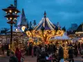 A lively Copenhagen Christmas market at dusk, with a brightly lit carousel and festive stalls. People stroll amongst decorated trees, enjoying the magical atmosphere.