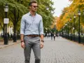 Eleganckie szare spodnie stylizacje na jesienny spacer. Mężczyzna w błękitnej koszuli i szarych spodniach, otoczony złotymi liśćmi.