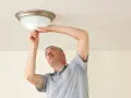 Mężczyzna wymienia żarówkę w lampie sufitowej, wykonując retrofit LED.