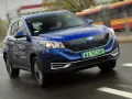 Niebieski Seres 3 jedzie po mokrej drodze, za nim widać autobus.