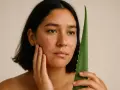 Donna con brufoli da stress sul viso, che tiene una foglia di aloe vera.