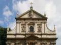 Bogata fasada kościoła w stylu barokowym, z rzeźbami i zdobieniami, pod błękitnym niebem.