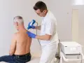 Therapeut behandelt Manns Schulter mit Stoßwellentherapiegerät. Es tut nicht weh, wie eine Spritze in die Schulter.