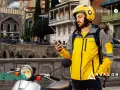 Kurier Glovo sprawdza telefon, gotowy do pracy w blokach czasowych. Na skuterze widnieje logo.