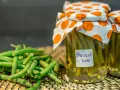 Fagiolini sott'olio in agrodolce, conservati in barattoli con tappi decorati. Freschi e pronti per essere gustati.