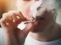 Persona fumando un cigarrillo, exhalando humo denso. Podría ser un indicio de sobredosis de nicotina.