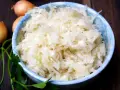 Schüssel mit frischem Krautsalat, daneben Zwiebeln und Petersilie. Perfekt für ein leckeres Krautsalat Rezept.