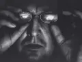 Portret Krzysztofa Gierałtowskiego w okularach, z dłońmi przy twarzy.