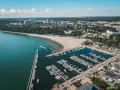 Widok z lotu ptaka na plażę miejską w Gdyni, z zatoką pełną jachtów i łodzi, oraz miastem w tle.
