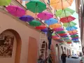 Kolorowe parasolki tworzą tęczowy dach nad uliczką w Tarnowie. Mężczyzna na drabinie dokańcza instalację.